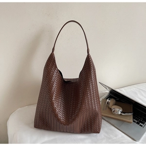 Macro view of dark brown woven leather hobo bag next to a laptop on a white desk