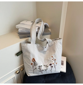 Detailed close-up of colorful floral embroidery on a grey canvas tote bag against books