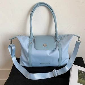 Detail of light blue nylon travel bag with crossbody strap on a geometric base