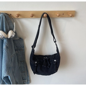 Detail of black denim crescent crossbody bag with multiple zippers on a wall hanger