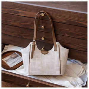 Detail of canvas tote bag with brown leather handles and brand logo patch