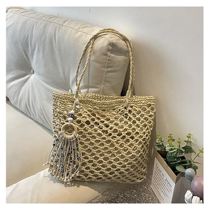 Detail of hollow woven beige straw tote bag with evil eye tassel on a sofa