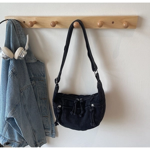 Detail of black denim crescent bag featuring front zipper pockets and adjustable strap