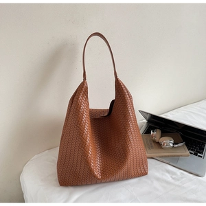 Detailed view of brown woven leather tote bag with a laptop and urban lifestyle props