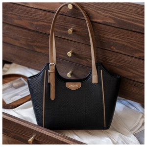Close-up of a vintage black tote bag with brown leather accents in a wooden drawer