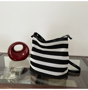 Dettaglio borsa tote in rete a righe bianche e nere con finiture in pelle su tavolo