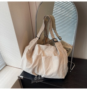 Detail of beige nylon tote bag with three front pockets and adjustable shoulder strap