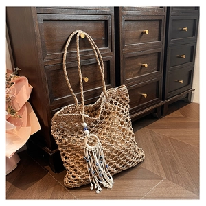 Detail of hollow woven straw tote bag with evil eye tassel charm on a wooden background
