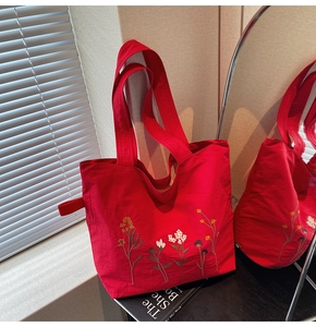 Detail of red canvas tote bag featuring vibrant floral embroidery and dual top handles