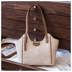 Detail of beige woven fabric tote bag with brown leather handles in a wooden drawer