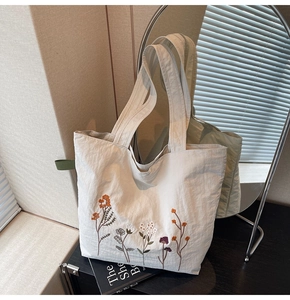 Detailed embroidery of colorful flowers on a cream canvas tote bag with woven texture