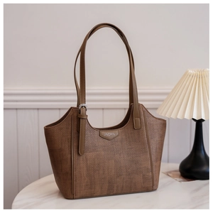 Close-up of brown textured tote bag with metal brand plaque on marble table