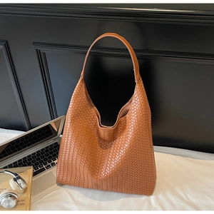 Close-up of brown woven leather hobo bag next to laptop and headphones on a desk