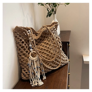 Detail of woven straw tote bag with evil eye tassel charm on a wooden surface
