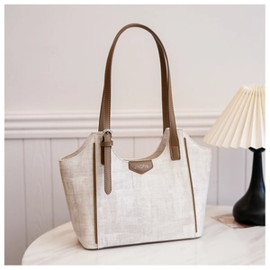 Detail of the trapezoidal tote bag showing beige canvas texture and brown leather straps