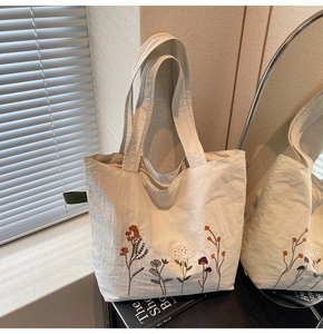 Detail of floral embroidery on off-white canvas tote bag with textured material