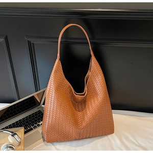 Detail of a brown woven leather hobo bag showing texture next to a laptop and books