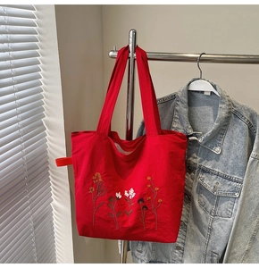 Detailed close-up of vibrant floral embroidery on a large red canvas tote bag