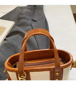 Detail of cream bucket bag with caramel leather handles and golden metal zipper hardware