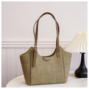 Detail of green woven tote bag with brown leather handles and silver brand plaque