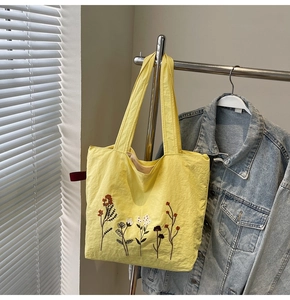 Detailed close-up of floral embroidery on a yellow canvas tote bag hanging near a jacket