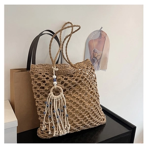 Detail of hollow woven straw tote bag with evil eye tassel charm and braided shoulder strap
