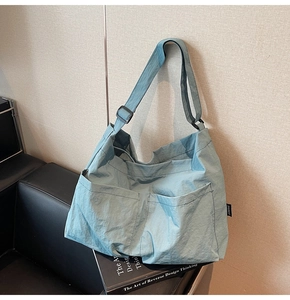 Detail of light blue nylon tote bag showing double front pockets and adjustable strap