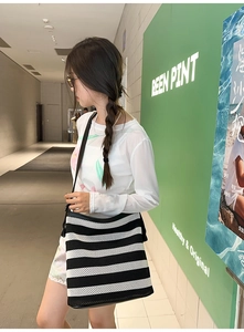 Vista laterale di una borsa tote in rete a righe bianche e nere indossata in un corridoio