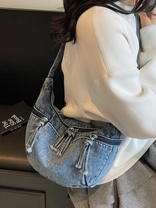 Washed blue denim crescent bag with decorative zippers and fringe for casual wear