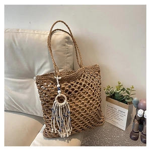 Detail of hollow woven straw tote bag with evil eye tassel charm and boho fringe accents