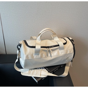 Détail du sac de sport crème avec fermetures noires et bandoulière sur surface en cuir