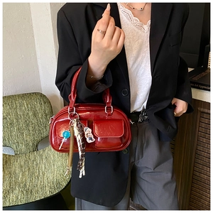 Dettaglio di una mini borsa Boston rossa lucida con ciondoli tenuta da una modella