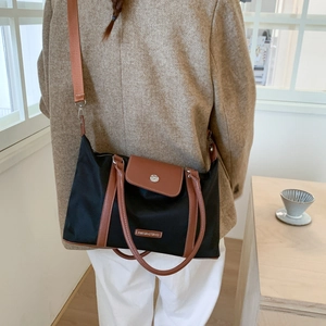 Detail of the black travel bag with brown leather handles worn by a female model