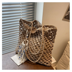 Close-up of hollow woven tote bag featuring a blue evil eye bead and white tassel detail