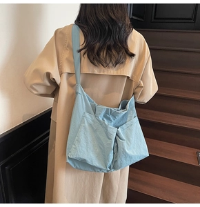 Detail of light blue canvas shoulder bag with dual large pockets shown in a city scene