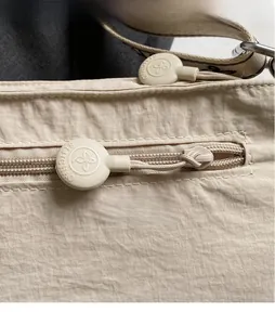 Detailed close-up of beige crossbody bag with circular rubber zipper pulls and textured nylon
