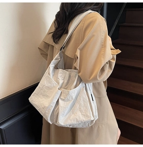 Detail view of white pleated nylon shoulder bag with large side pocket on female model