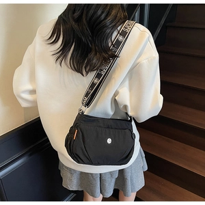 Detail of black nylon crossbody bag with orange side ribbon and patterned wide strap