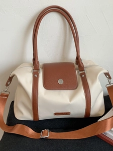 Minimalist beige travel bag with brown leather accents and adjustable shoulder strap