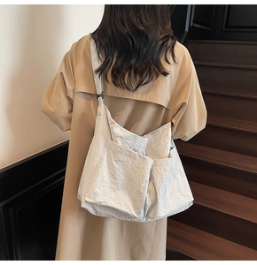 Detail of white pleated crossbody bag with wide shoulder strap on khaki trench coat