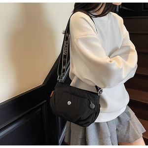 Detail view of black nylon crossbody bag featuring a wide logo strap and silver badge emblem