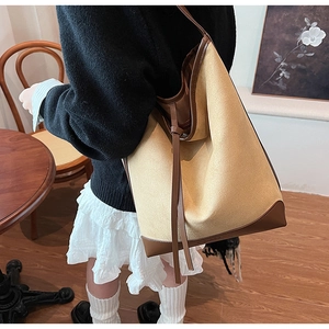 Detailed view of spacious yellow canvas tote bag with brown leather trim shown on shoulder