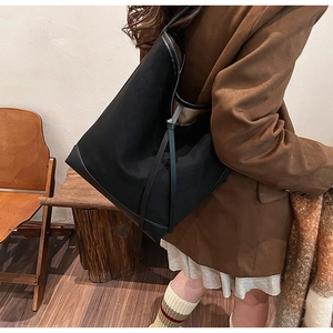 Detail of a large black suede tote bag with stylish knotted thin shoulder straps