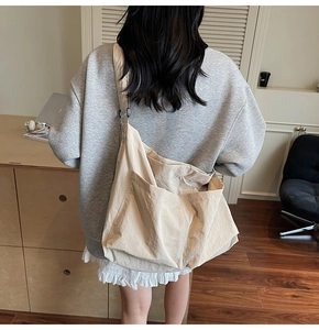 Back view of a casual beige canvas messenger bag worn by a model in a cozy home setting