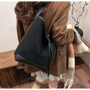Detail view of large black canvas tote bag featuring premium leather patchwork and fringe