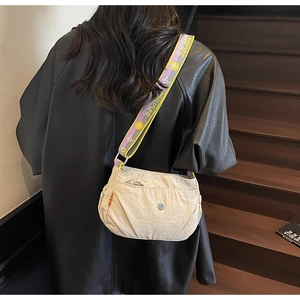 Detail view of beige crossbody bag with patterned wide strap on a wooden staircase