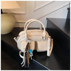 Dettaglio borsa a bauletto bianco crema con doppie tasche, finitura lucida e ciondolo