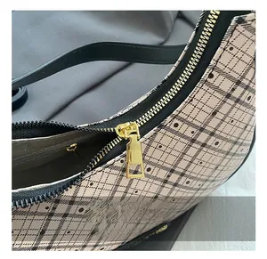 Close-up of golden zipper and hardware on beige plaid pattern crescent shoulder bag