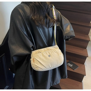 Close-up of beige nylon crossbody bag with woven strap and metal logo on stairs