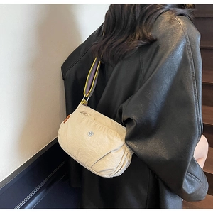 Close-up of beige nylon crossbody bag featuring a vibrant tricolor woven shoulder strap